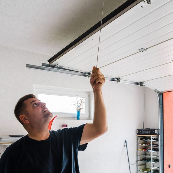 a man is holding a string in a kitchen. features garage door services garage door repair garage door installation garage door spring repair provided by Retrak Door Service.