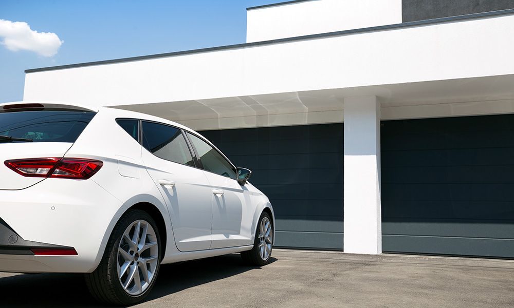 This scene from Lakewood, CO shows a white car parked in front of a white building. with features such as garage door services garage door repair garage door installation garage door spring repair.